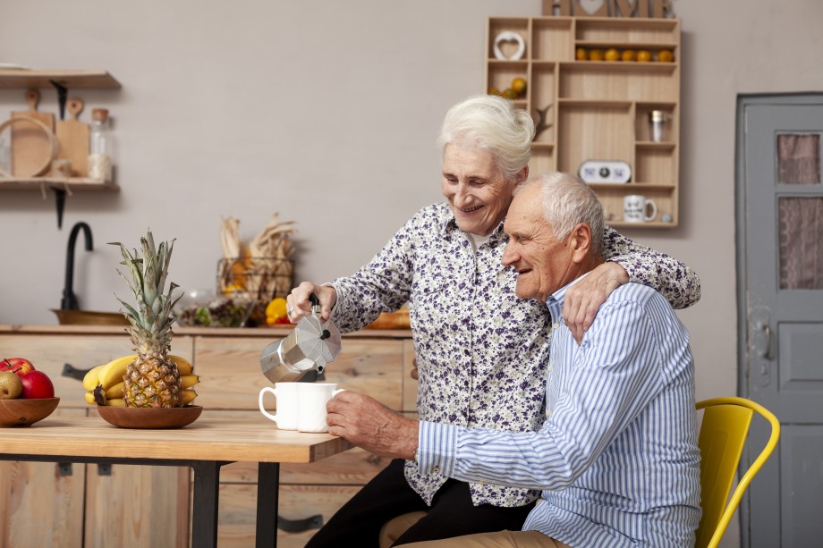 Älteres Paar sitzt in der Küche, die Frau schenkt Kaffee ein.