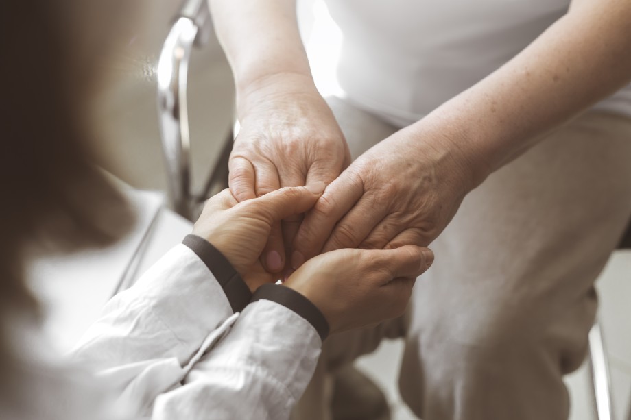 Pflegekraft hält beruhigend die Hände einer älteren Person.